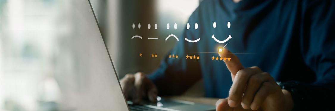 Eine unbekannte Person sitzt vor einem Laptop und wählt zwischen Emotionsdarstellungen aus