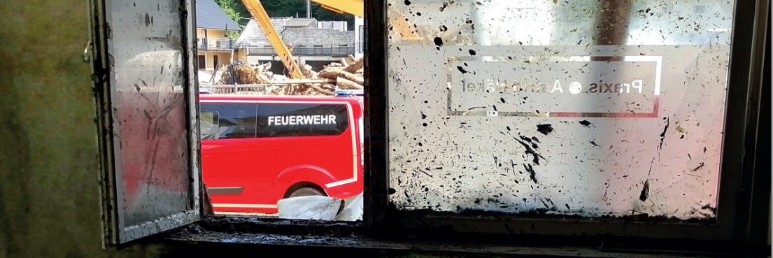 Blick durch ein schmutziges Fenster auf ein rotes Feuerwehrfahrzeug mit weißer Aufschrift 'FEUERWEHR'.