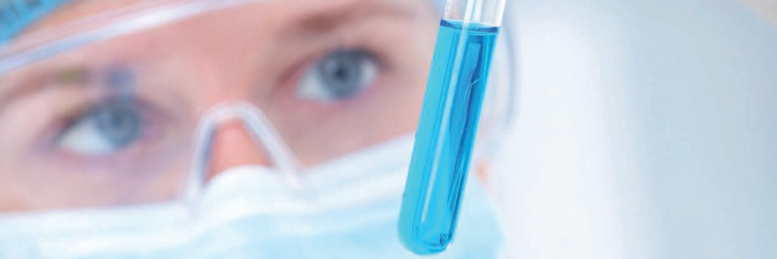 Hand hält Reagenzglas mit blauem Flüssigkeit vor Laborgerät, im Hintergrund unscharfe Laborumgebung, Textteil 'FORSCHUNG' sichtbar.