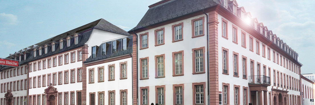 Fassade des Eltzer Hofes mit weißem Putz, roten Fensterrahmen und Mansarddach an einer Straßenecke bei Tageslicht.